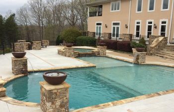 A residential house with an outdoor swimming pool with a hot tub and water features installed by Premier Pool Enterprises
