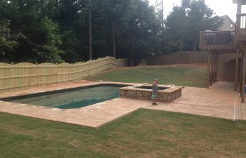 A happy little boy by a backyard swimming pool with a hardscaped hot tub installed by Premier Pool Enterprises