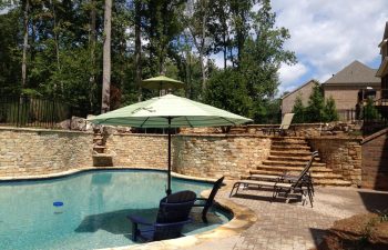 A backyard hardscaped patio with an outdoor swimming pool installed by Premier Pool Enterprises