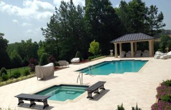A backyard stone patio with a swimming pool and a hot tub installed by Premier Pool Enterprises