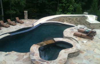 Outdoor furniture by an outdoor swimming pool and a hot tub installed on a flagstone patio.