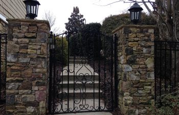A metal fencing with a gate between hardscaped stone posts