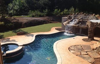 Backyard swimming pool with a hot tub and hardscaped waterfall installed by Premier Pool Enterprises