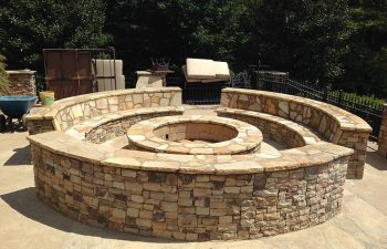 A stone fire pit with hardscaped benches around it built by Premier Pool Enterprises