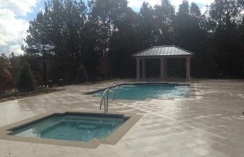 A backyard stone patio with a swimming pool and a hot tub installed by Premier Pool Enterprises