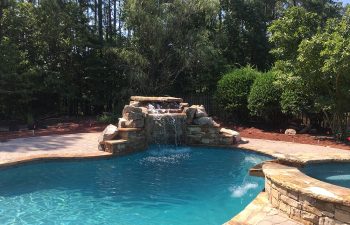 Backyard swimming pool with a hot tub and hardscaped waterfall installed by Premier Pool Enterprises