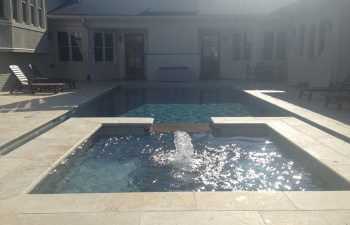 A residential house with an outdoor swimming pool with a hot tub and water features installed by Premier Pool Enterprises