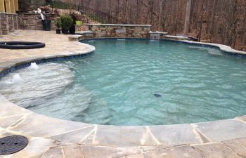 Backyard swimming pool with hardscaped water features installed by Premier Pool Enterprises