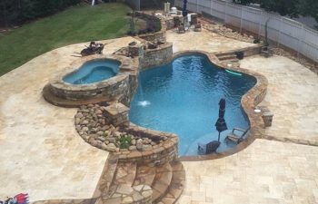 Garden stone patio with an outdoor kitchen and hardscaped swimming pool with a hot tub built by Premier Pool Enterprises