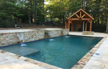 Backyard swimming pool with a hardscaped hot tub and waterfalls installed by Premier Pool Enterprises