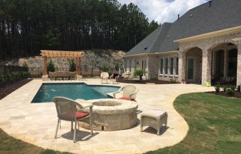 A residential house with backyard stone patio with a fire pit and a swimming pool.