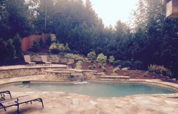A backyard hardscaped swimming pool with a hot tub and flagstone deck installed by Premier Pool Enterprises
