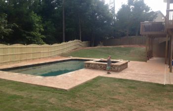 A happy little boy by a backyard swimming pool with a hardscaped hot tub installed by Premier Pool Enterprises