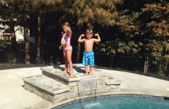 Happy kids playing by a backyard swimming pool with water features installed by Premier Pool Enterprises