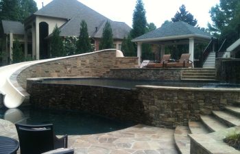 An outdoor hardscaped swimming pool with a slide and a flagstone patio.