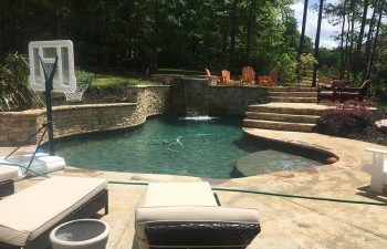 An outdoor furniture on a backyard stone patio with a spa and swimming pool installed by Premier Pool Enterprises