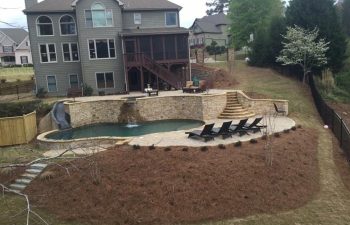 A big residential house with a backyard stone patio with an outdoor spa and swimming pool designed and installed by Premier Pool Enterprises