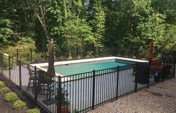 A fenced backyard swimming pool with a stone deck.