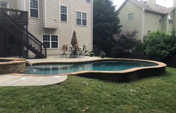 A residential stucco home with a backyard swimming pool with a hot tub and a waterfall.
