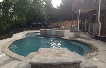 Backyard swimming pool with a hot tub and water features installed by Premier Pool Enterprises