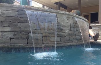 Backyard swimming pool with water features installed by Premier Pool Enterprises