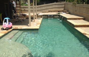 Backyard swimming pool with water features and stone deck.