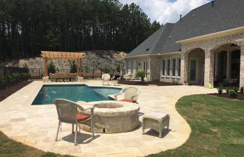 A brick house with a stone garden patio with a fire pit and a swimming pool.