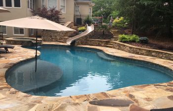 Backyard swimming pool with hot tub and flagstone deck installed by Premier Pool Enterprises