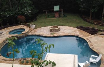 Garden stone patio with a fire pit by a swimming pool with a hot tub and a waterfall.