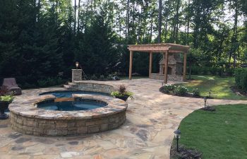 Garden flagstone patio with a stone fireplace and an outdoor spa built by Premier Pool Enterprises