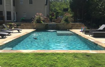 Outdoor furniture on a stone deck of a backyard swimming pool with a waterfall installed by Premier Pool Enterprises