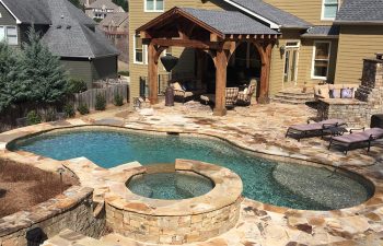 A residential house with flagstone patio with a swimming pool and hot tub.