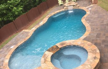 Backyard flagstone patio with a swimming pool with hot tub and waterfall installed by Premier Pool Enterprises