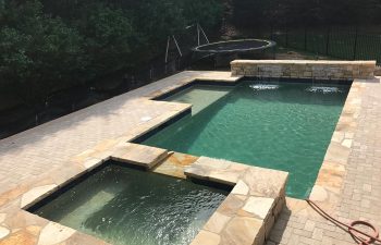 Backyard modern swimming pool with hot tub and water features installed by Premier Pool Enterprises