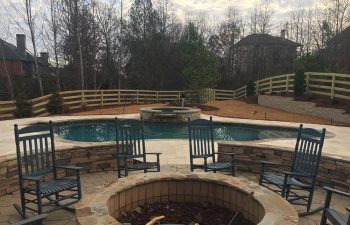Backyard stone patio with a fire pit by a swimming pool with hot tub installed by Premier Pool Enterprises