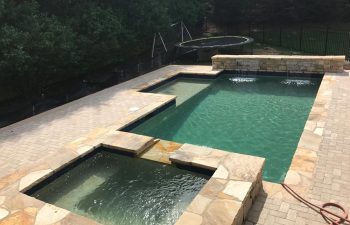 Backyard modern swimming pool with hot tub and water features installed by Premier Pool Enterprises