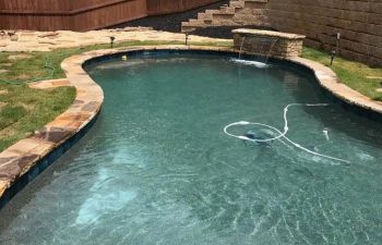 Backyard swimming pool with a hardscaped waterfall installed by Premier Pool Enterprises