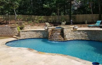 Backyard swimming pool with hardscaped hot tub and water features installed by Premier Pool Enterprises
