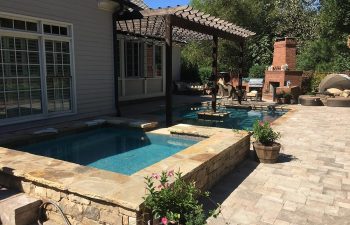 A patio with outdoor fireplace and swimming pool with hot tub installed by Premier Pool Enterprises.