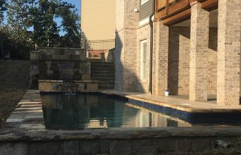 Backyard swimming pool with hardscaped waterfall installed by Premier Pool Enterprises