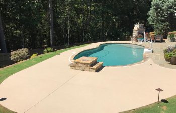 A patio with an outdoor fireplace by a backyard swimming pool installed by Premier Pool Enterprises.