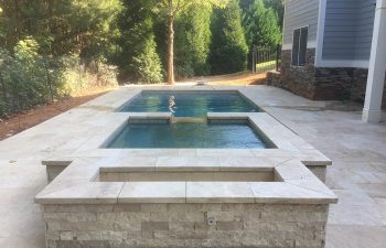 Backyard swimming pool with hot tub and stone deck.