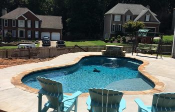 Backyard swimming pool with hardscaped waterfall installed by Premier Pool Enterprises.
