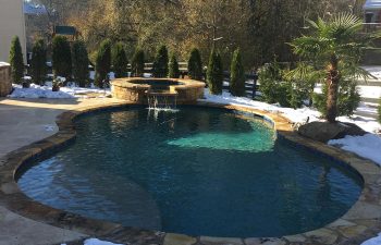 Backyard swimming pool with hot tub installed by Premier Pool Enterprises in winter.