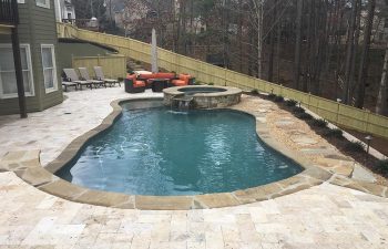 Backyard swimming pool with a hot tub and stone deck with garden furniture on it.
