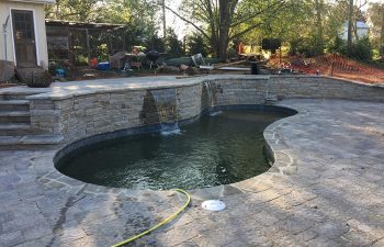 backyard pool with hardscaped water features and paver deck.
