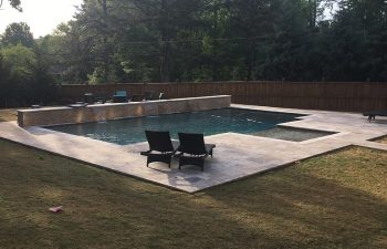 pool chairs on a deck of a modern backyard pool with water features