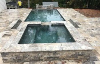 backyard swimming pool with hot tub and water features and stone paver deck