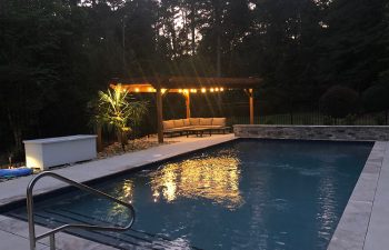an outdoor living space with cozy sitting places and lights placed by a backyard swimming pool
