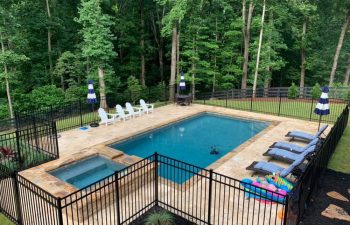 Pool furniture on a fenced backyard flagstone deck by swimming pool with a hot tub